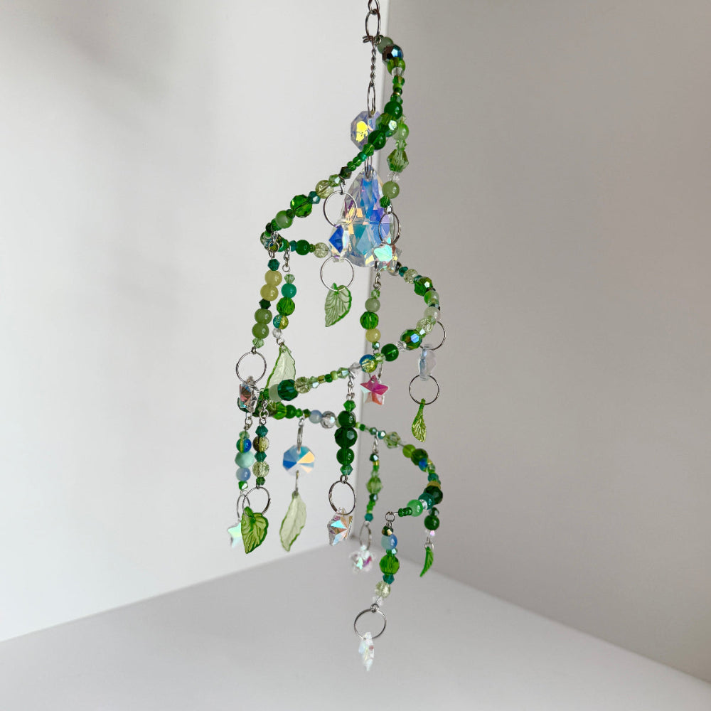 Decorative hanging mobile with green beads and leaf elements on a neutral background