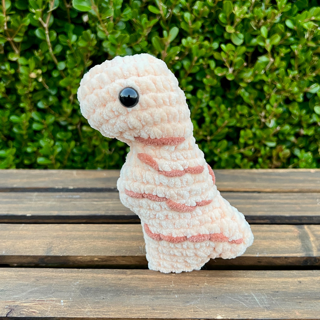 Crocheted dinosaur t-rex dino nugget grilled on a wooden surface with green foliage in the background