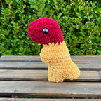 Crocheted dinosaur t-rex dino nugget with ketchup dipped head on a wooden surface with green foliage in the background