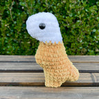 Crocheted dinosaur t-rex dino nugget with ranch dipped head on a wooden surface with green foliage in the background