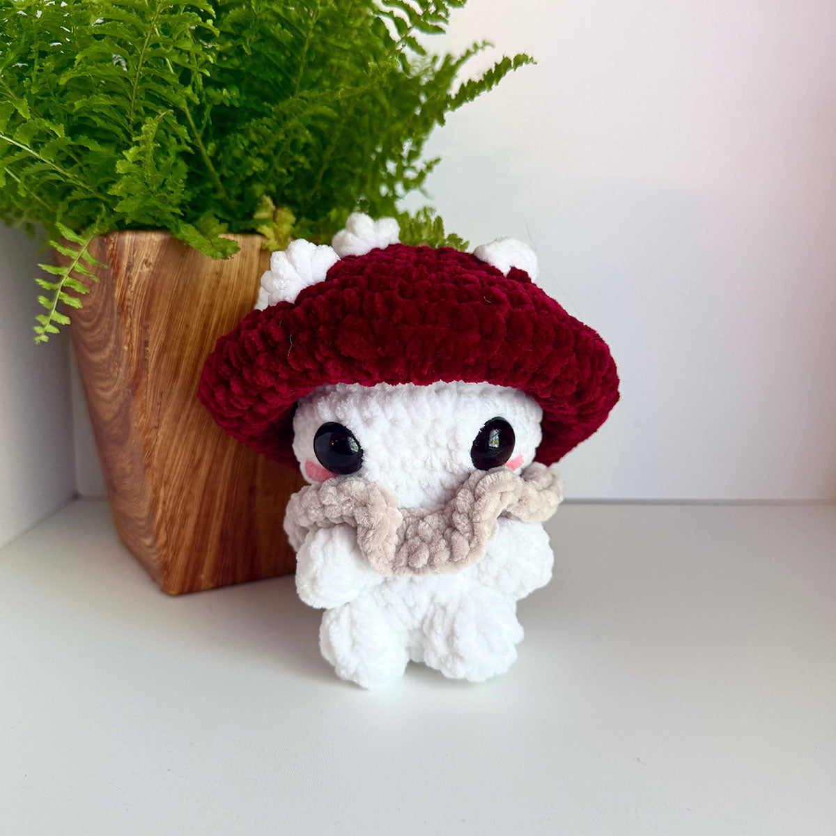 Crocheted mushroom plush toy with a red cap and white body on a light surface.