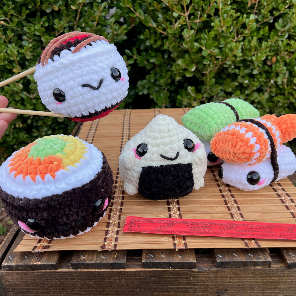 Plush sushi toys on a wooden surface with a hand holding chopsticks.